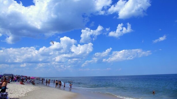 Une plage où l’on voit des gens nager et bronzer sous un ciel dégagé.