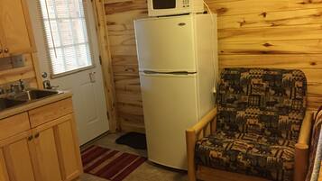 A compact kitchen with a refrigerator, a microwave, a sink, and wooden cabinets.