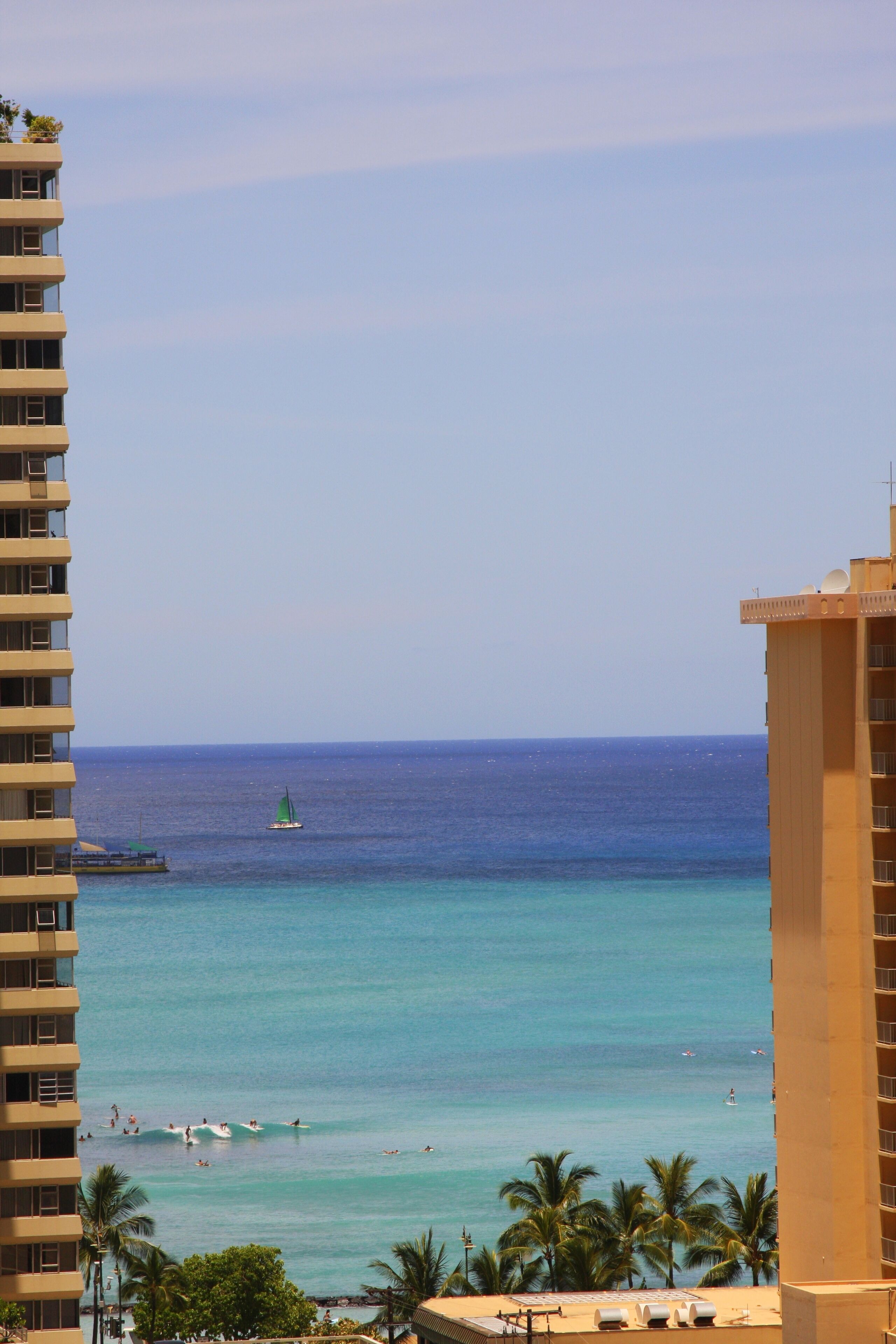 Un hotel moderno con vistas a una playa de aguas azules cristalinas, palmeras y un velero.