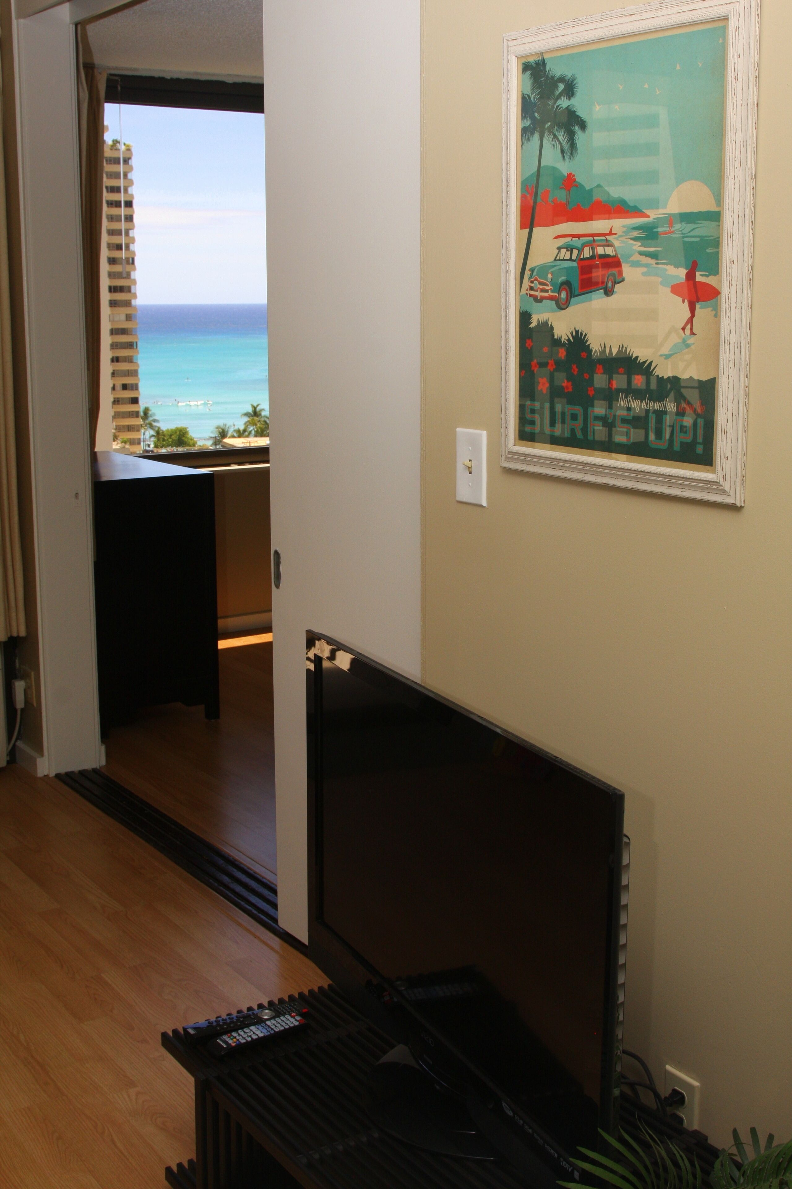A room with a view of the ocean, a framed poster on the wall, and a desk with a computer.