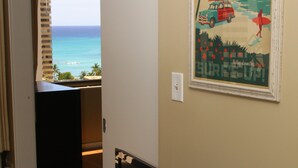 A room with a view of the ocean, a framed poster on the wall, and a desk with a computer. - Waikiki Banyan, Ocean-view 1BR apt: Full kitchen, FREE PARKING, NO RESORT FEES. (Honolulu)