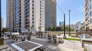 A rooftop patio with outdoor seating and a view of tall buildings. - Waikiki Banyan, Ocean-view 1BR apt: Full kitchen, FREE PARKING, NO RESORT FEES. (Honolulu)