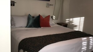 Een slaapkamer met een bed, kussens, een dekbed, een nachtkastje, een wandklok en een schilderij.