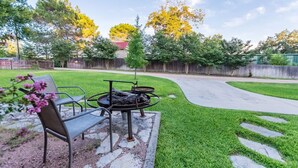 Un jardin avec un barbecue, une chaise et un chemin dallé.