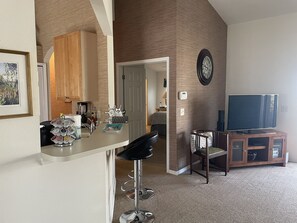 A modern kitchen with wooden cabinets, a built-in oven, and a coffee station. There is a dining area with a high chair and a TV on a wooden stand. - 3 Bedroom Home HEATED Pool WEBER Grill Located Right on the 7th Golf Hole (Palmetto)
