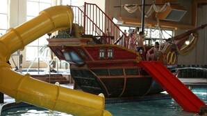 Parque acuático interior con zona de juegos temática de barco pirata y toboganes.