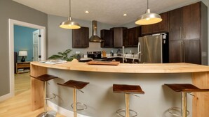 Una cocina moderna con armarios de madera oscura, un refrigerador de acero inoxidable, una isla curva de madera con taburetes e iluminación colgante.