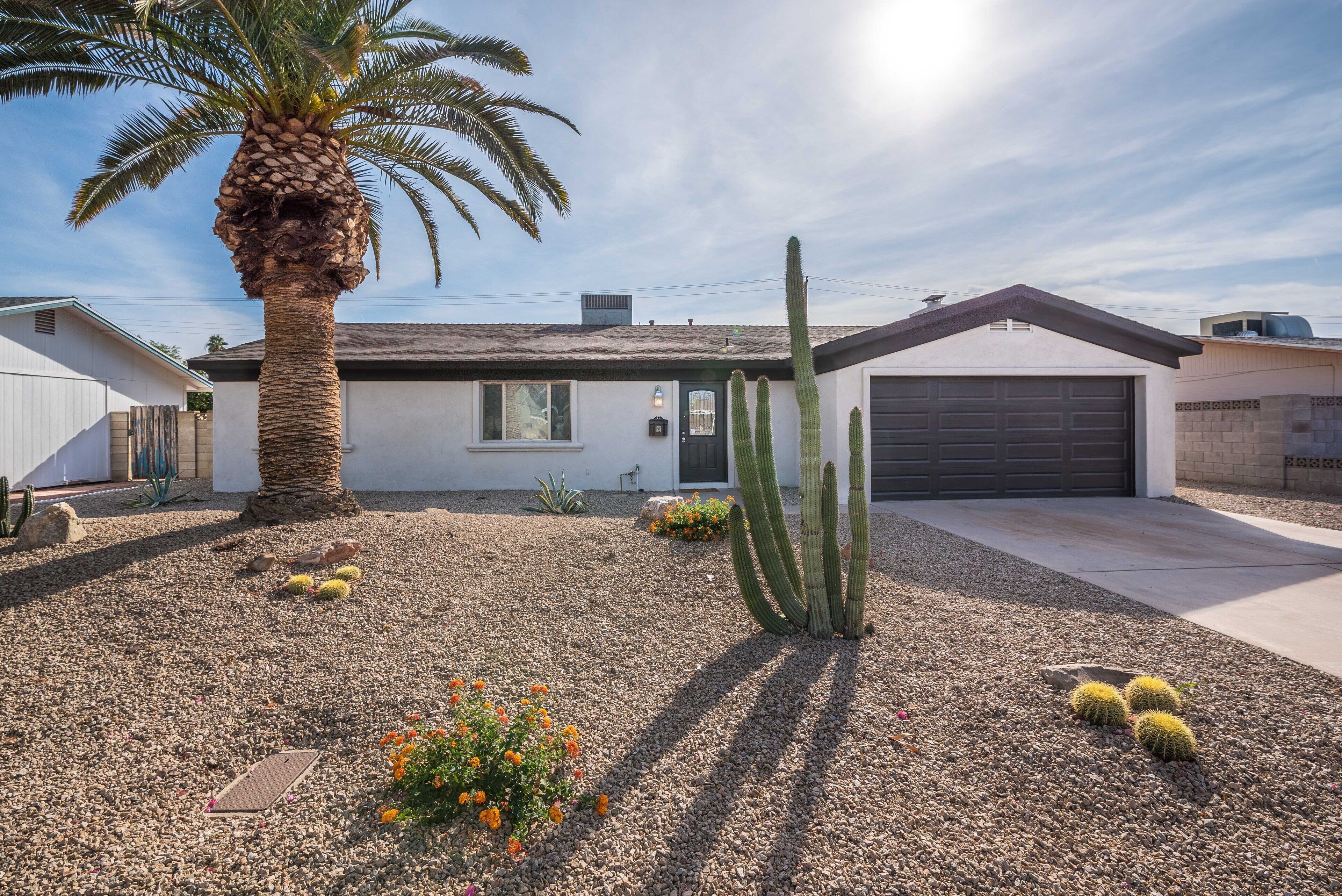 Una casa con garaje, una palmera y cactus en el jardín delantero.