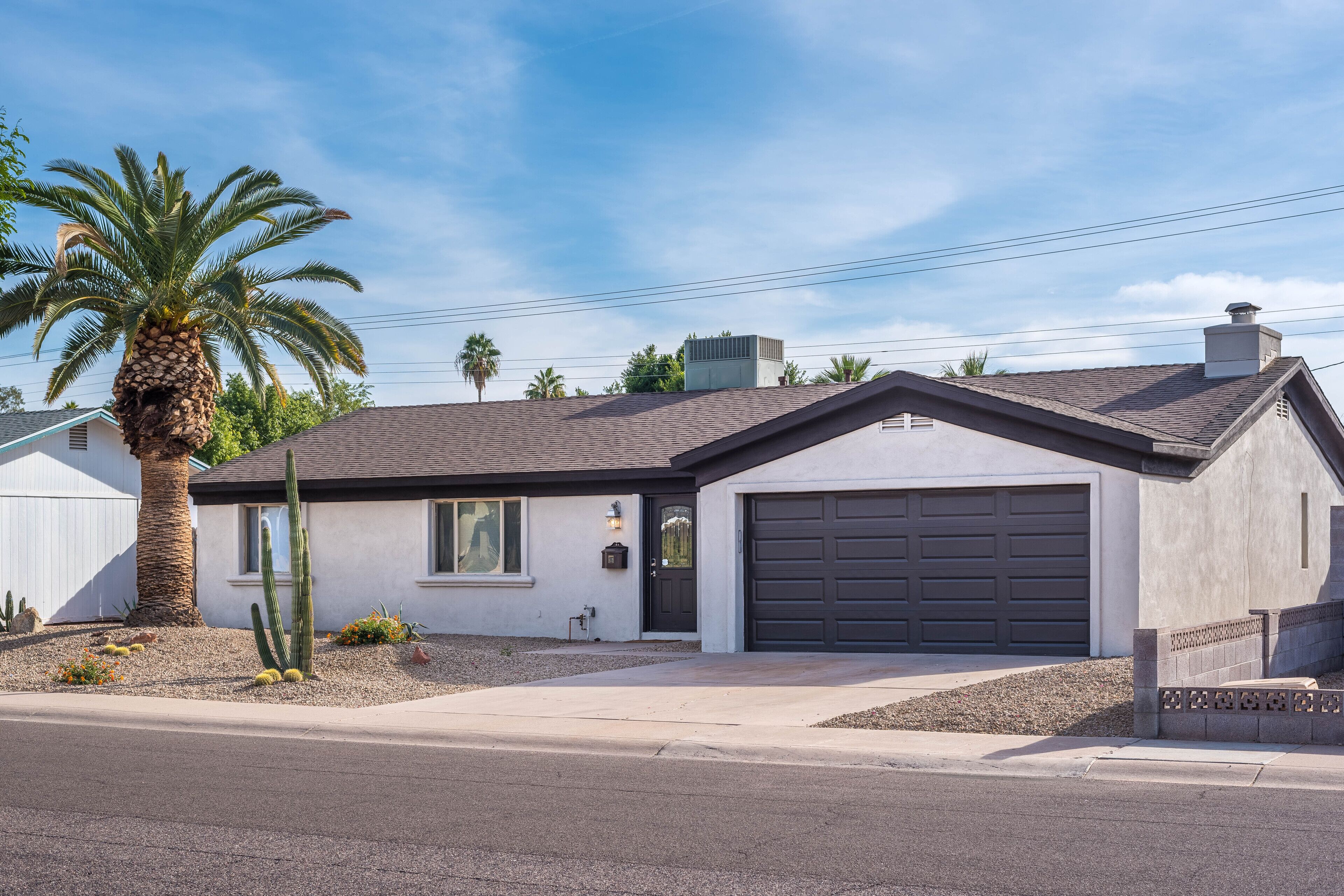 A single-story house with a dark-colored garage, a small front porch, and a palm tree.