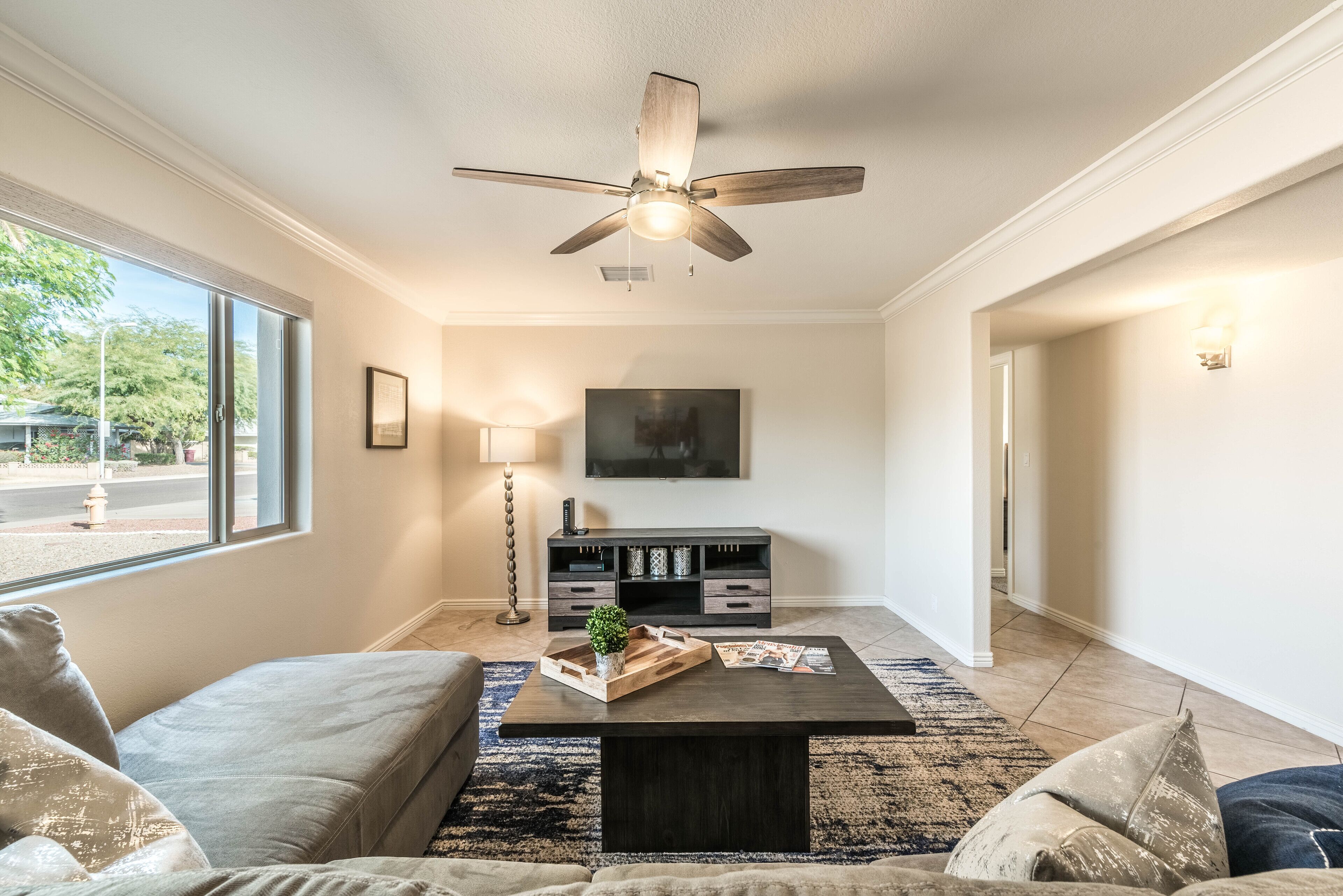 A living room with a ceiling fan, a coffee table with decorative items, a sofa, and a TV mounted on the wall.