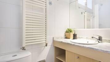 Un baño moderno con inodoro blanco, toallero, lavabo con encimera de mármol y espejo sobre el lavabo.