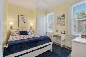 Une chambre à coucher comprenant un lit, des tables de chevet, un bureau, une chaise et des œuvres d’art accrochées aux murs.