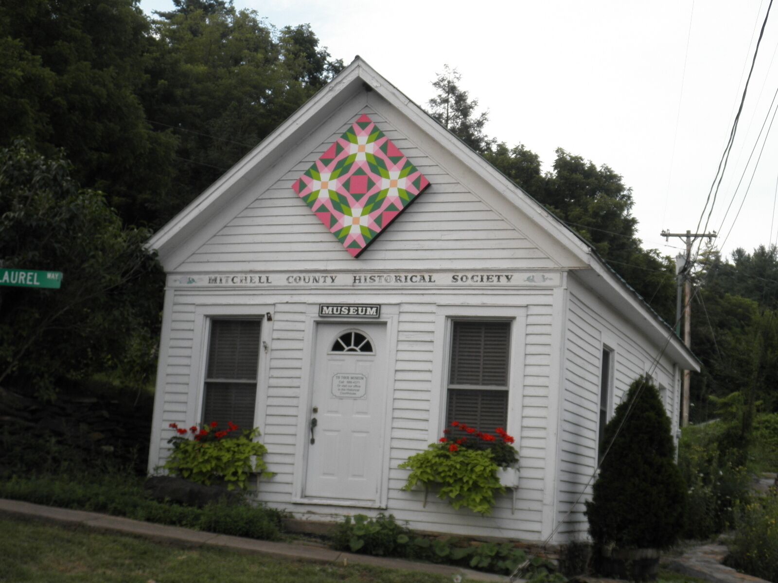 A small white building with a diamond-shaped quilt on the roof, labeled as the Mitchell County Historical Society Museum.