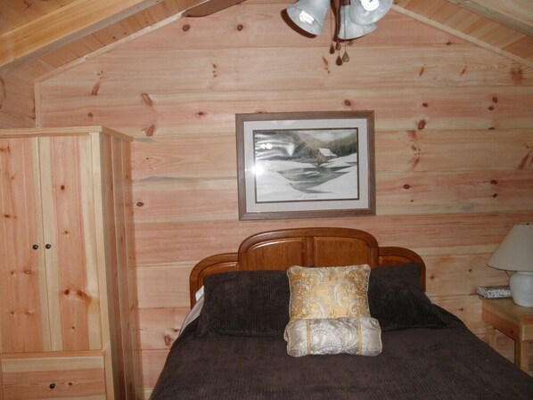 A cozy wooden cabin room with a bed, a nightstand, and a framed picture on the wall.