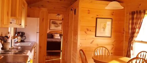 Ein Holzblockhaus-Interieur mit Küche, Essbereich und einem Bett.