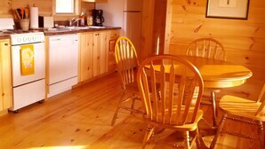 L’intérieur d’un chalet en bois comprend un coin cuisine, une table à manger en bois et des chaises.
