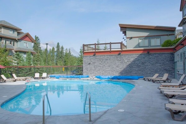 A swimming pool with lounge chairs, a stone wall, and a wooden deck.