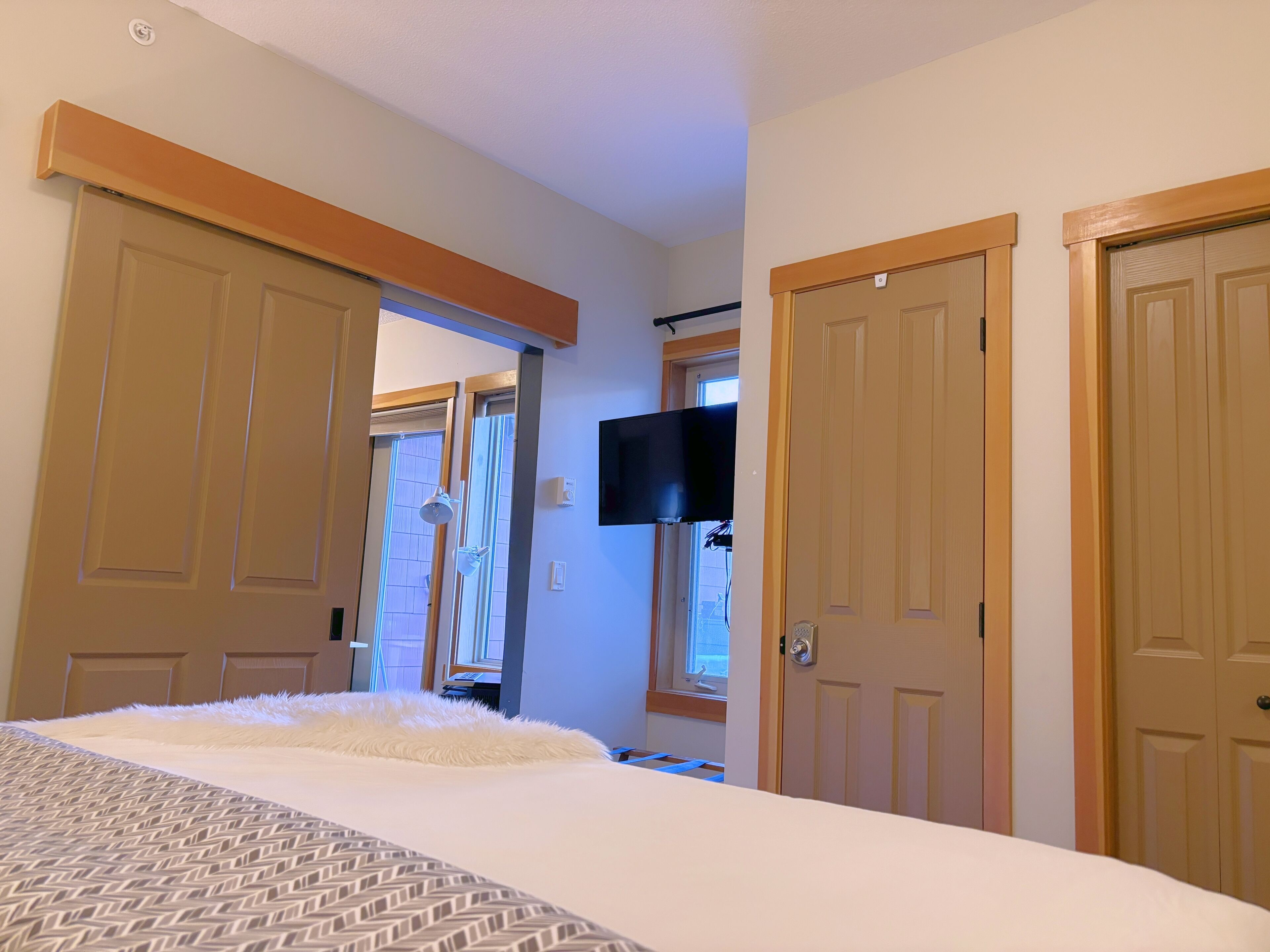A hotel room with a large bed, a flat-screen TV mounted on the wall, and two doors leading to other rooms.