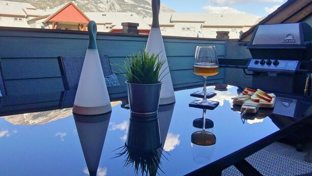 Una mesa con una copa de vino, una planta y comida, con montañas al fondo.