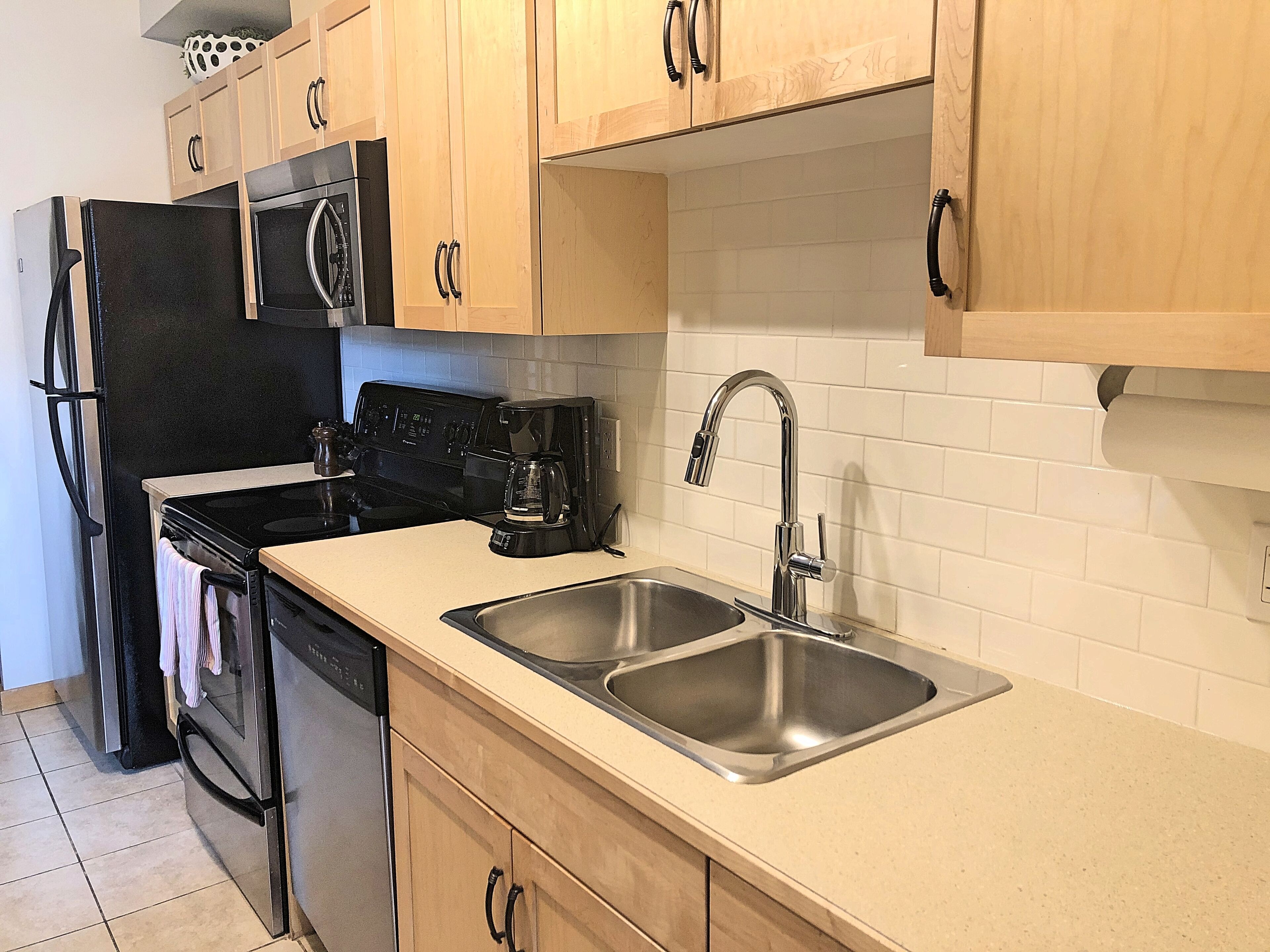 A kitchen with wooden cabinets, a stainless steel sink, a coffee maker, and a dishwasher.