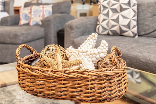 Ein Korbwannen auf einer Glastisch in einem Wohnzimmer mit grauen Sofas und gemusterten Kissen.