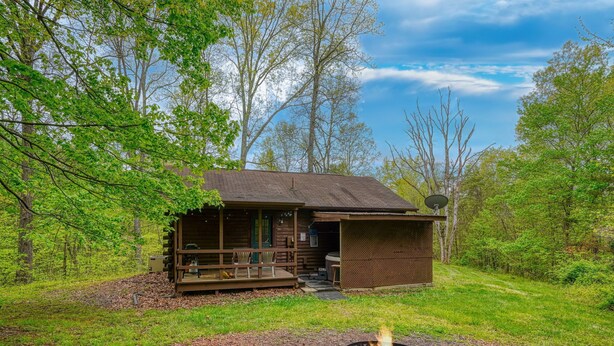 Een rustieke chalet met een veranda, een vuurkuil en een satellietantenne.