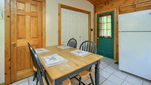 A dining area with a wooden table and chairs, a green door, and a white refrigerator.