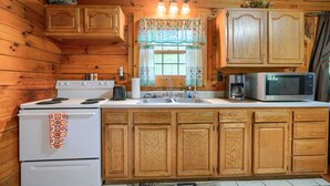 A wooden cabin kitchen with a stove, sink, microwave, and cabinets.