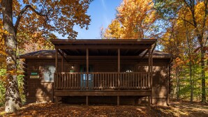 A wooden cabin with a porch, surrounded by trees with autumn leaves.