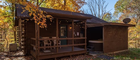 A rustic cabin with a porch, a hot tub, and a covered outdoor seating area.