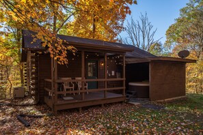 A rustic cabin with a porch, a hot tub, and a satellite dish.