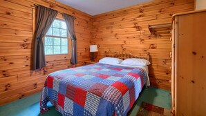Een kamer met houten lambrisering, een bed, een raam met gordijnen, een nachtkastje en een lamp.