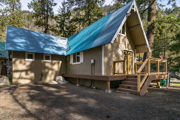 A cabin with a blue roof, wooden exterior, and a small porch with steps leading to a door.
