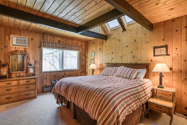 A wooden room with a bed, dresser, and window.
