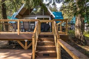 A wooden deck leading to a cabin with a blue roof, surrounded by trees. - Icicle Riverhaus-Cozy Riverfront Cabin Leavenworth (Leavenworth)
