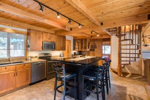 A modern kitchen with wooden cabinets, a central island with bar stools, stainless steel appliances, and a spiral staircase. - Icicle Riverhaus-Cozy Riverfront Cabin Leavenworth (Leavenworth)