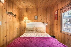 A wooden-paneled room with a bed, a lamp, and a window with a view.