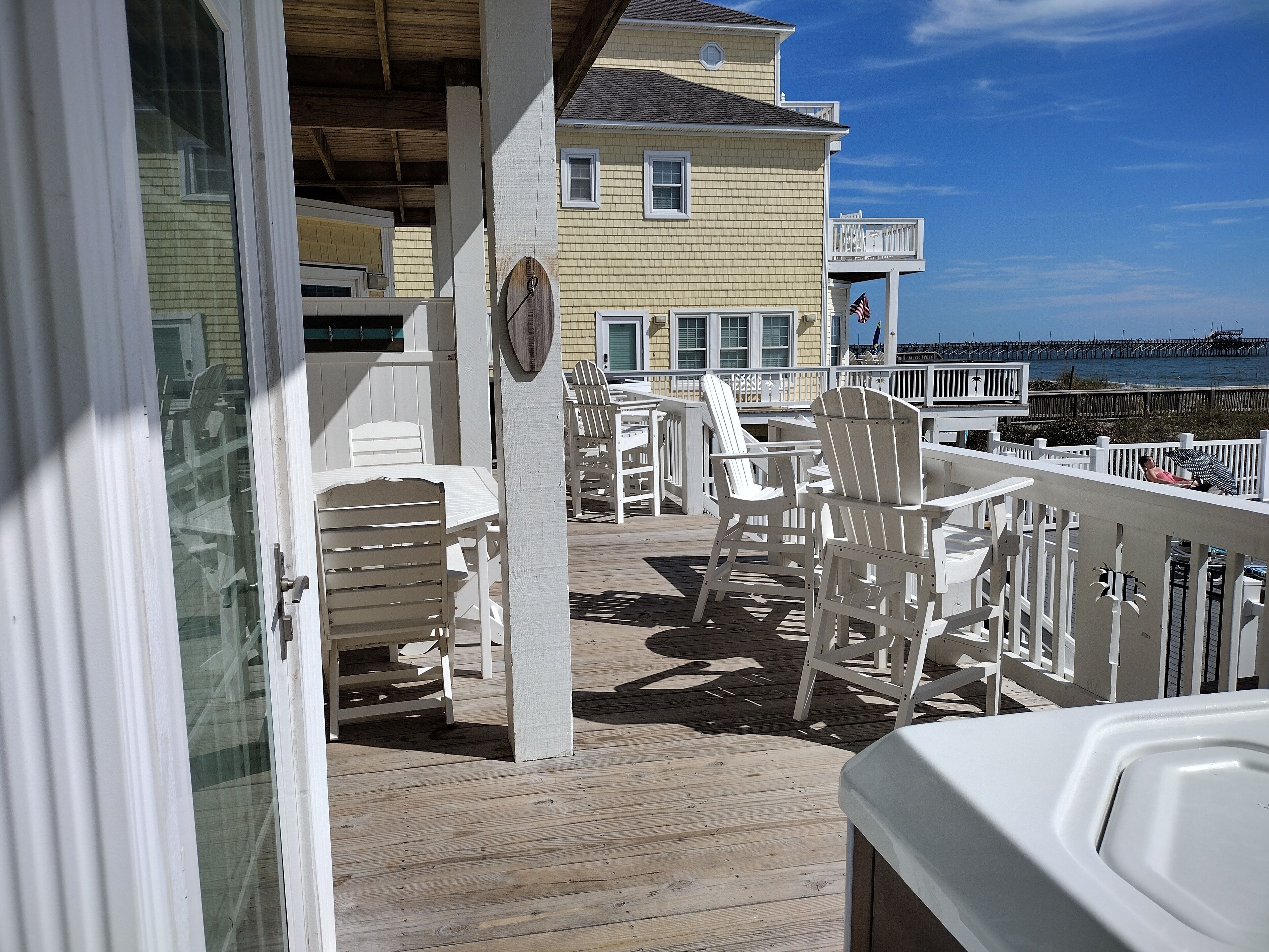 A wooden deck with white chairs and tables, overlooking a pier and the ocean.