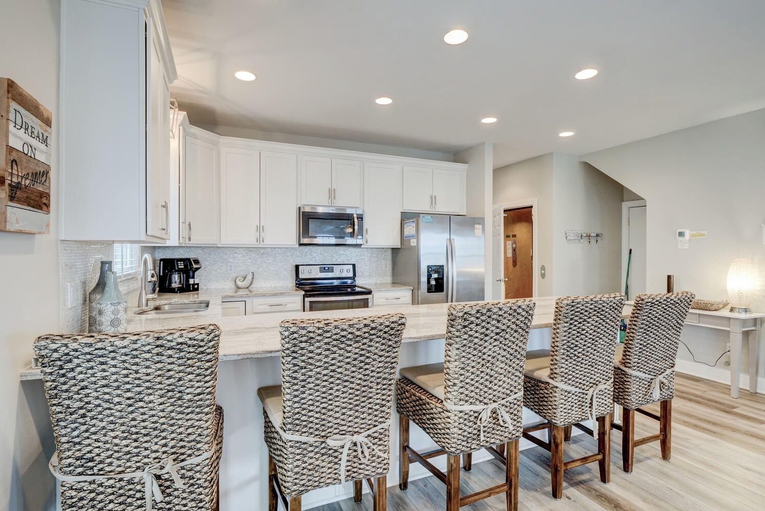 Una cocina moderna con armarios blancos, electrodomésticos de acero inoxidable y una isla central con taburetes de estilo barra.