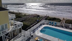 Área de piscina com vista para o oceano e a praia, deck de madeira e espreguiçadeiras.