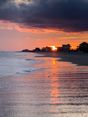 En strand med huse i baggrunden under solnedgang.