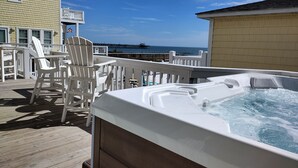 Um terraço com hidromassagem, cadeiras Adirondack brancas e vista para o oceano.