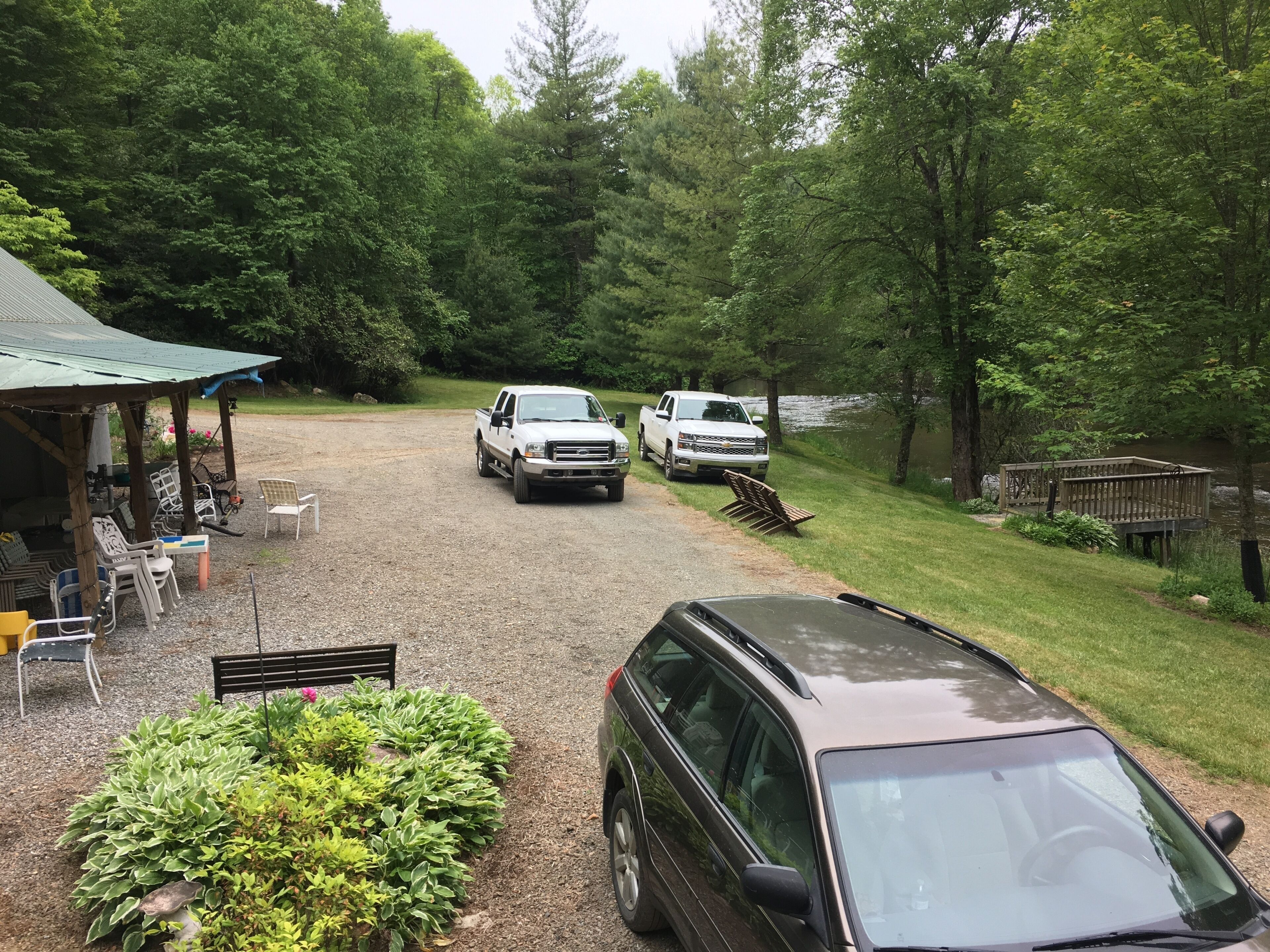 A gravel driveway leading to a white pickup truck parked near a covered outdoor seating area with chairs and tables.