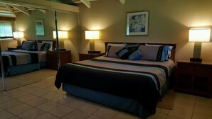Quarto de hotel com uma cama grande, duas mesas de cabeceira, um espelho e um quadro na parede.