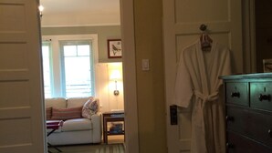A room with a bed, a dresser, a robe hanging on the door, and a window with blinds. - Lavender House Cottages, Classic Elegance in a Country Cottage (Point Reyes Station)