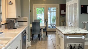 Een keuken met een centraal eiland, een eethoek met stoelen, een plafondventilator en uitzicht door de glazen deur.