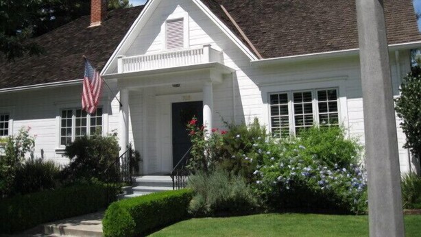 Een wit huis met twee verdiepingen, een veranda, schoorsteen en een Amerikaanse vlag.