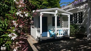 Een klein wit huisje met een veranda, een blauwe stoel en een tuin vol witte bloemen.
