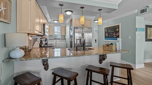 A kitchen with a central island, bar stools, pendant lights, and a refrigerator. - Oceanfront! Private Beach Access. Prime location, building A-main pool & complex (Indian Beach)