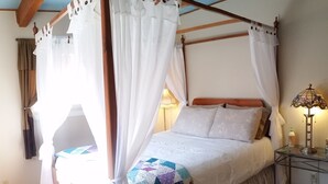 A bedroom with a four-poster bed, white curtains, a quilt, a bedside lamp, and a nightstand. - Little Park Road Retreat - Hot Tub with a View (Grand Junction)